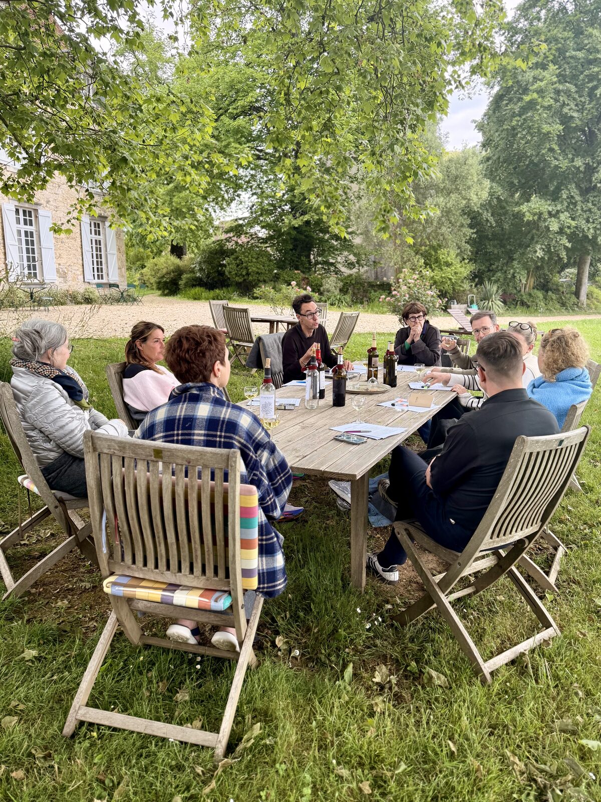 Gruppe an einem langen Holztisch im Garten des Châteaus, das Haus im Hintergrund.